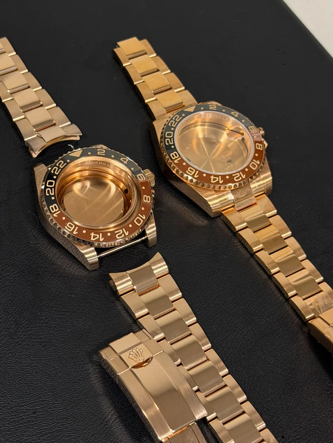 Two rose gold GMT watch cases and bracelets laid out mid-process before reassembly